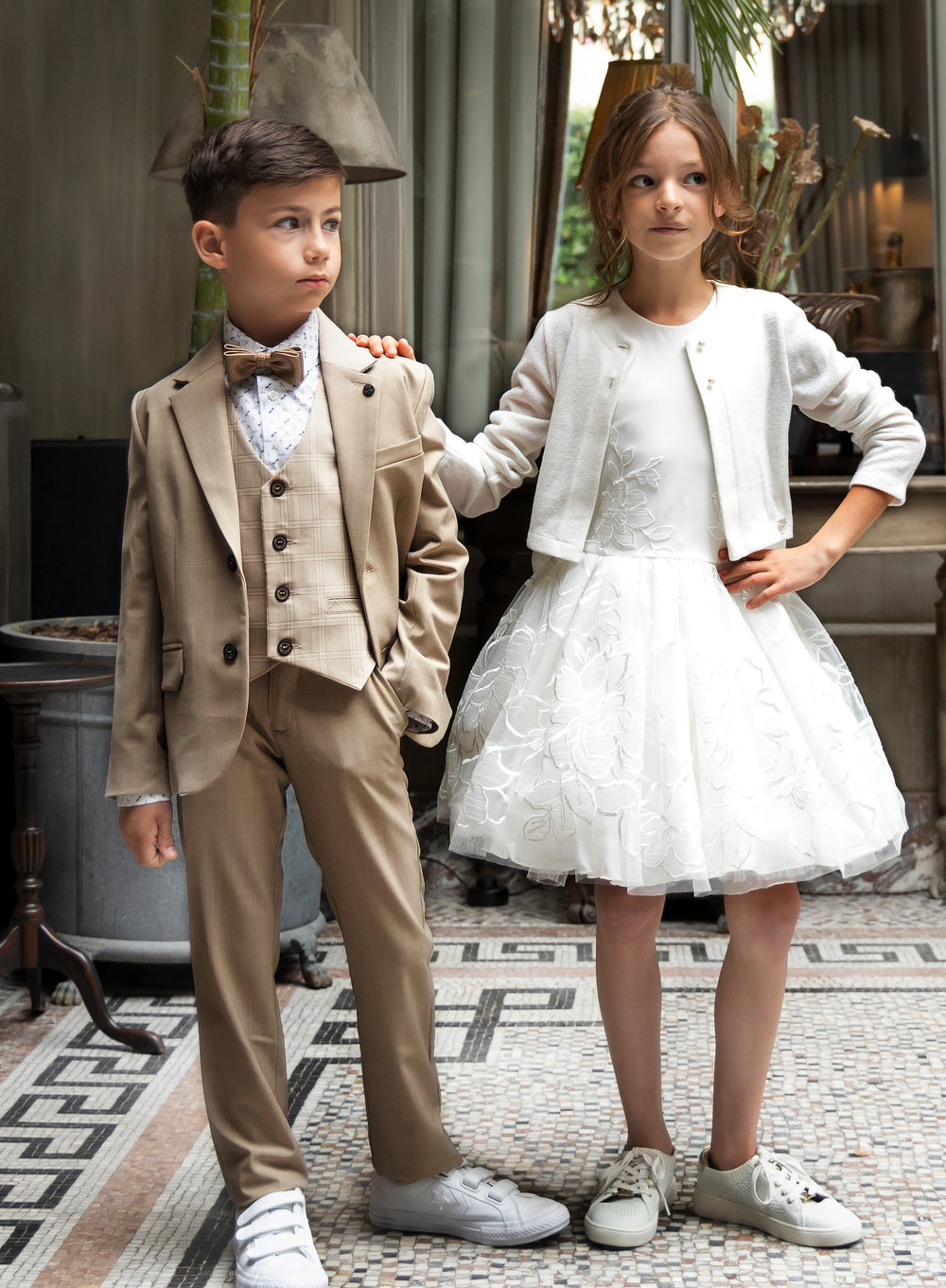 Stijlvol beige kostuum voor jongens en een witte tule jurk met fijne details voor meisjes